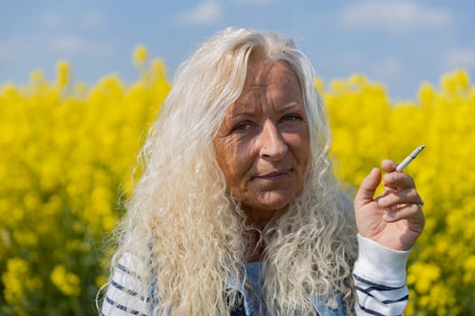 Elderly Woman smoke a cigarette in rape field with yellow blossums