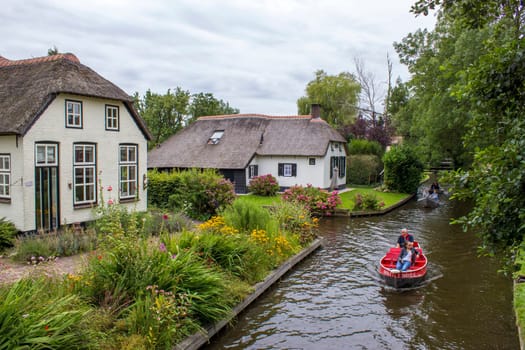 GIETHOORN, NETHERLANDS - AUGUST 01 2017: Unknown visitors in the sightseeing boating trip in a canal in Giethoorn. The beautiful houses and gardening city is know as "Venice of the North""."