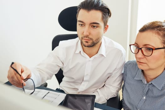 Two business people discussing financial data looking at computer screen. Entrepreneurs working hard sitting at computere screen in office. People having deadline working together. Workmates talking about project