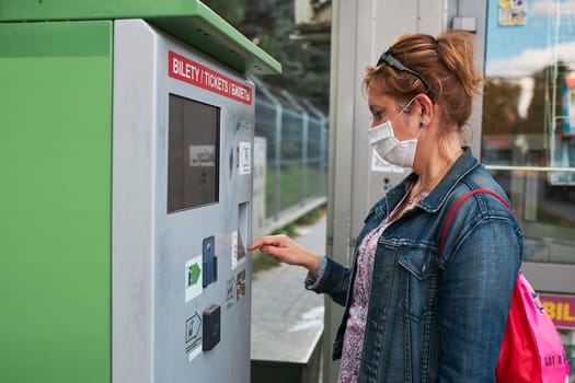 Woman buying bus ticket in ticket machine wearing face mask to cover mouth and nose traveling during pandemic coronavirus outbreak