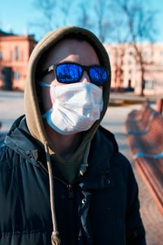 Young man in the hood wearing the face mask to avoid virus infection and to prevent the spread of disease. Walking in city centre. Virus infection protection. Real people, authentic situations