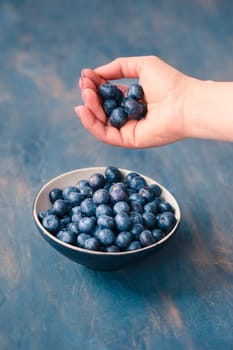 Woman putting freshly gathered blueberries into a small bowl. Table painted in blue in the background