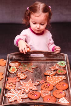 Little girl placing Christmas gingerbread cookies on wooden tray