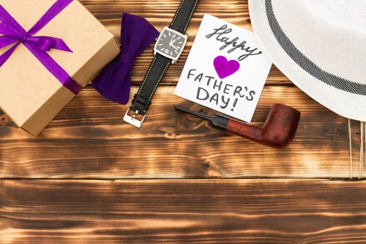 Greeting card Happy Father's Day with a gift box and men's accessories on a rustic wooden tabletop. Flat lay.Copy space