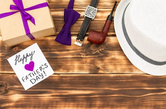 Greeting card Happy Father's Day with a gift box and men's accessories on a rustic wooden tabletop. Flat lay. Top view. Copy space