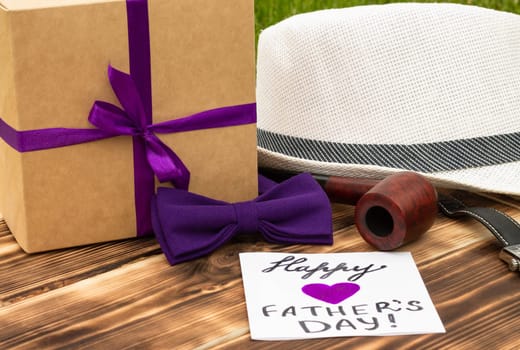 Greeting card Happy Father's Day with a gift box and men's accessories on a rustic wooden tabletop