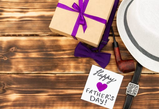 Greeting card Happy Father's Day with a gift box and men's accessories on a rustic wooden tabletop. Flat lay. Top view. Copy space