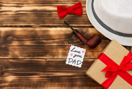 Greeting card Love You Dad with a gift box and men's accessories on a rustic wooden tabletop. Flat lay. Top view. Copy space.