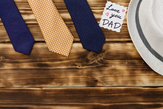 Greeting card Love You Dad with a gift box and men's accessories on a rustic wooden tabletop. Flat lay. Top view. Copy space.