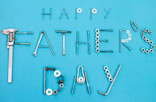 Text Happy Father's Day lined with bolts, nuts, wrenches and other construction tools on a blue background. Flat lay. Top view