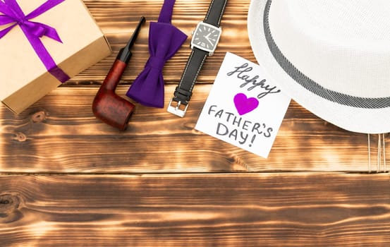 Greeting card Happy Father's Day with a gift box and men's accessories on a rustic wooden tabletop. Flat lay. Top view. Copy space