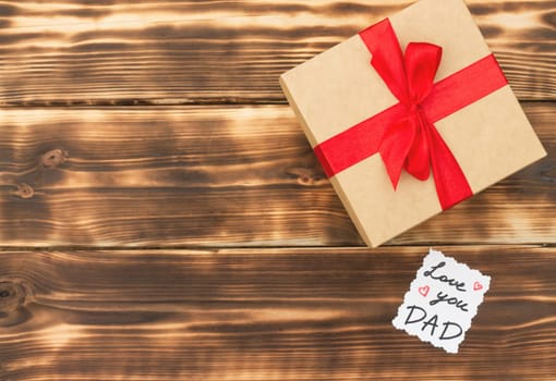 Greeting card Love You Dad with a gift box on a rustic wooden tabletop. Flat lay. Top view. Copy space