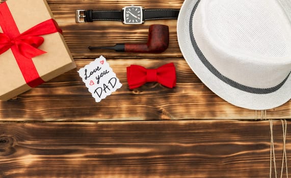 Greeting card Love You Dad with a gift box and men's accessories on a rustic wooden tabletop. Flat lay. Top view. Copy space.