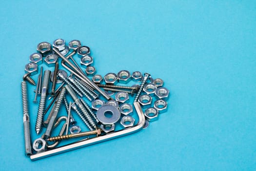 Heart laid out of bolts, nuts, wrenches and other construction tools on a blue background. Father's day concept. Copyspace