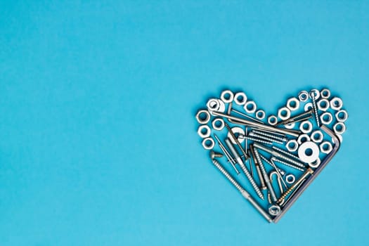 Heart laid out of bolts, nuts, wrenches and other construction tools on a blue background. Father's day concept. Flat lay. Top view. Copyspace