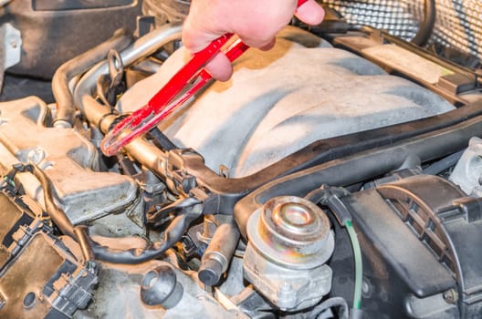 Hand of an auto mechanic in the engine compartment in the car repair workshop..