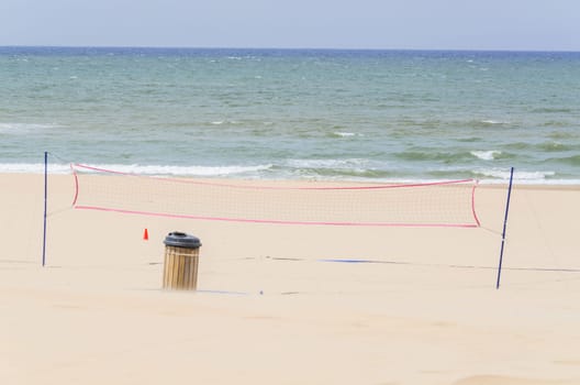 Beach a volleyball net in the background the blue sea and a cloudless sky..