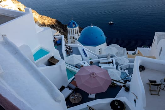 Oia, Santorini, Greece - June 28, 2021: View from viewpoint of Oia village with blue dome of  greek orthodox Christian church and traditional whitewashed greek architecture.  Santorini, Greece