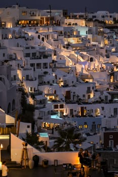 Imerovigli, Santorini, Greece - July 1, 2021: Illuminated whitewashed houses with terraces and pools and a beautiful view in Imerovigli on Santorini island, Greece