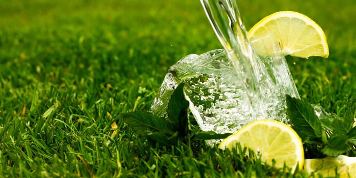 Glass of sparkling water or lemonade with lemon and mint leaves. Water with splashes and drops flows into a glass. Banner.