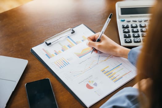 Woman accountant writing on business paper marketing statistic and data, Asian businesswoman working with paperwork charts and graphs and calculator, summary report planner, accounting concept