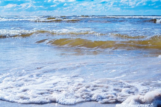 Bright blue sky with white clouds almost merges with sea waves with foam rolling on shore. Meditation and relaxation. Wonderful moments. Tourism and travel. Splendor of nature. Rest and pleasure.