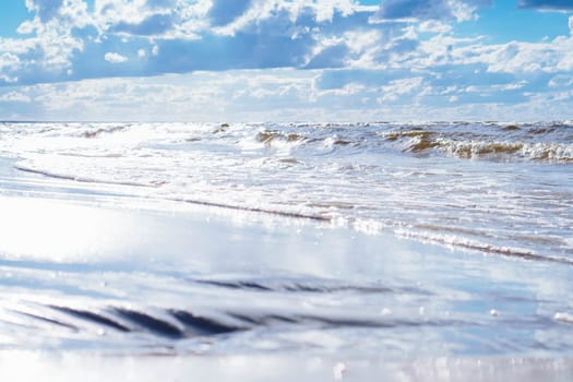Blue sky with white clouds almost merges with sea waves with foam rolling on shore. Meditation and relaxation. Interior paintings. Wonderful moments of life. Tourism and travel. Rest and pleasure.