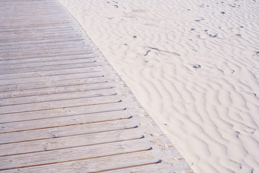 Wooden walkway on beach for walking is located on white sand. Walking along coast in fresh air. Comfort and relaxation. Tourism and travel. Relaxation and meditation. Loneliness and peace.