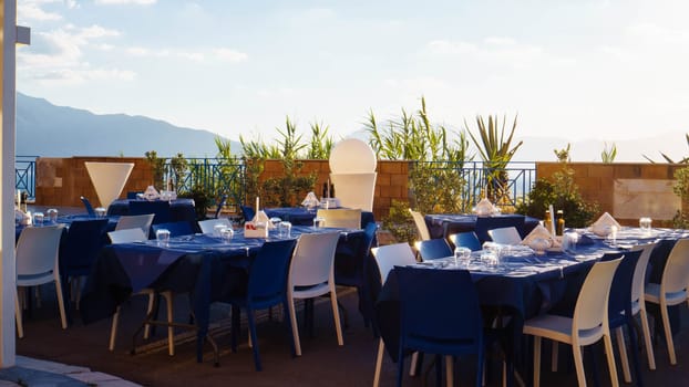 Restaurant, cafe on outdoor terrace with view of sky and mountains. Tables set with blue linen and white dishes. Italian style. Tourism and travel. Enjoying life. Beautiful places.