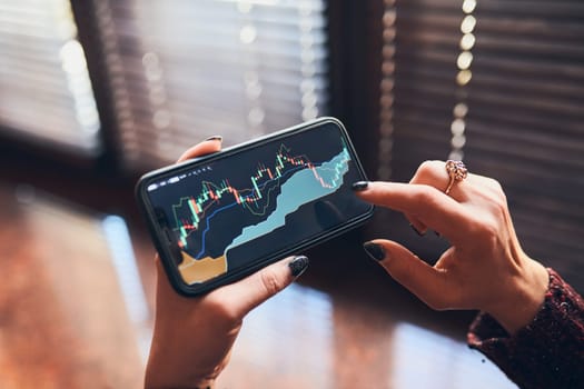Person investing trading on stock cryptocurrency market using investing application on smartphone. Stock market investment in hand. Trader holding mobile phone looking at candle chart