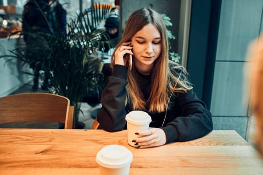Young woman talking on the phone at cafe, having a pleasant phone call, answering call, chatting by mobile phone with friend while sitting in a cafe and drinking coffee. Girl relaxing in cafe