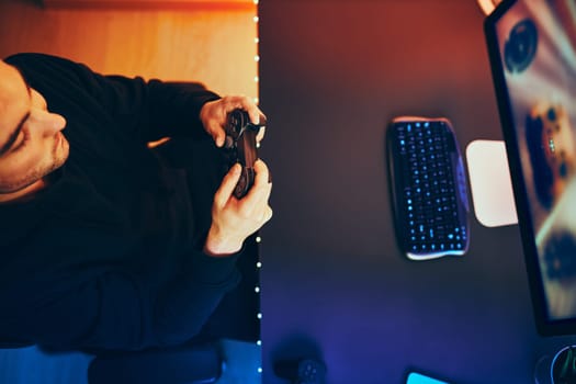 Man playing video game at home. Gamer holding gamepads sitting at front of screen. Streamer playing online in dark room lit by neon lights. Competition and having fun