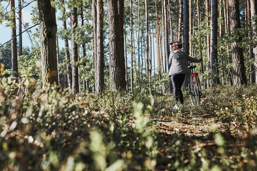 Active woman cycling on forest road. Female riding bicycle off-road route on summer vacation day. Woman wearing bicycle helmet and gloves