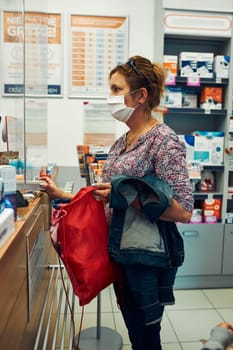 Woman shopping at pharmacy, buying medicines, wearing face mask to cover mouth and nose during pandemic coronavirus outbreak