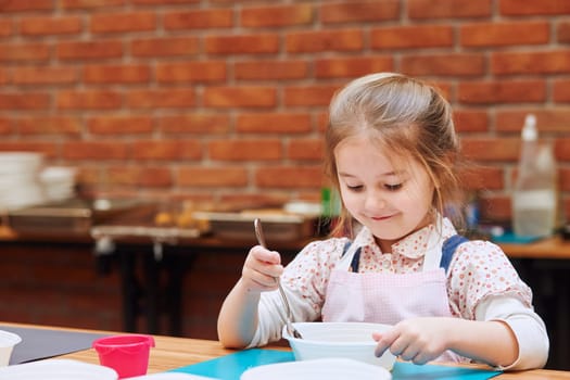 Happy, smiling little girl stirring the yolk with sugar. Kid taking part in baking workshop. Baking classes for children, aspiring little chefs. Learning to cook. Combining and stirring prepared ingredients. Real people, authentic situations