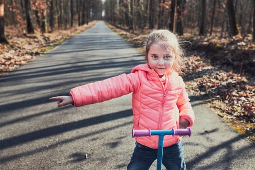 Little girl playing in the park, riding a scooter, having fun on sunny autumn day. Real people, authentic situations