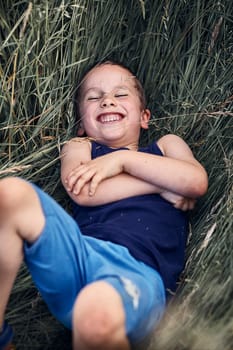 Little happy smiling boy playing in a tall grass in the countryside. Candid people, real moments, authentic situations