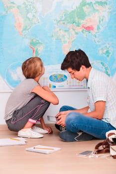Teenagers learning in a classroom sitting on a floor by a map of the world