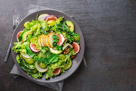 Fresh green leafy salad with fruits and nuts on grey table background. Concept for a tasty and healthy meal