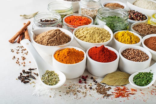 Colorful herbs and spices for cooking meal. Indian and Asian spices On white stone background closeup