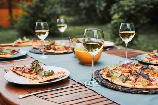 Dinner in a home garden. Pizza, salads, fruits and white wine on table in a orchard in a backyard