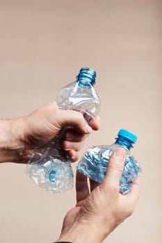 Male hand holding squashed plastic bottle over paper background. Collecting plastic waste to recycling. Concept of plastic pollution and too many plastic waste. Copy space at the top