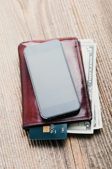 Smartphone with blank screen, wallet, dollar banknotes, debit credit cards and notebook on wooden table. View from above. Portrait orientation