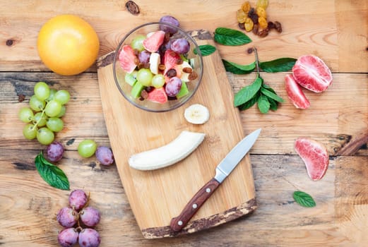 Making fruit salad with grapes, banana, grapefruit, kiwi and mint leaves