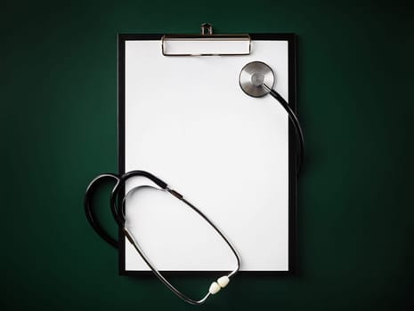 Blank clipboard with stethoscope on green background. Flat lay.
