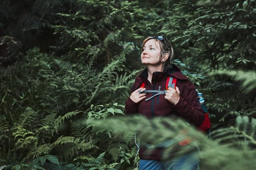 Woman with backpack hiking in forest, actively spending summer vacation close to nature. Woman walking on path among trees