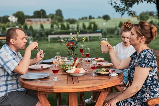 Family having a meal from grill during summer picnic outdoor dinner in a home garden. Close up of people sitting at a table with food and dishes