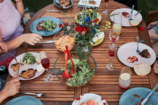 Family having a meal from grill during summer picnic outdoor dinner in a home garden. Close up of people sitting at a table with food and dishes