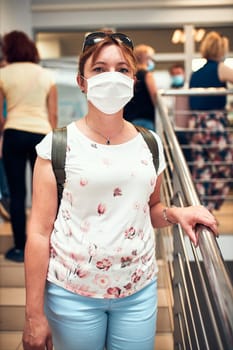 Woman going downstairs in public place inside wearing face mask to cover mouth and nose during pandemic coronavirus outbreak