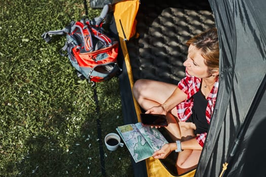 Woman planning next trip while sitting with map in tent. Woman relaxing in tent at camping during summer vacation. Actively spending vacations outdoors close to nature. Concept of camp life
